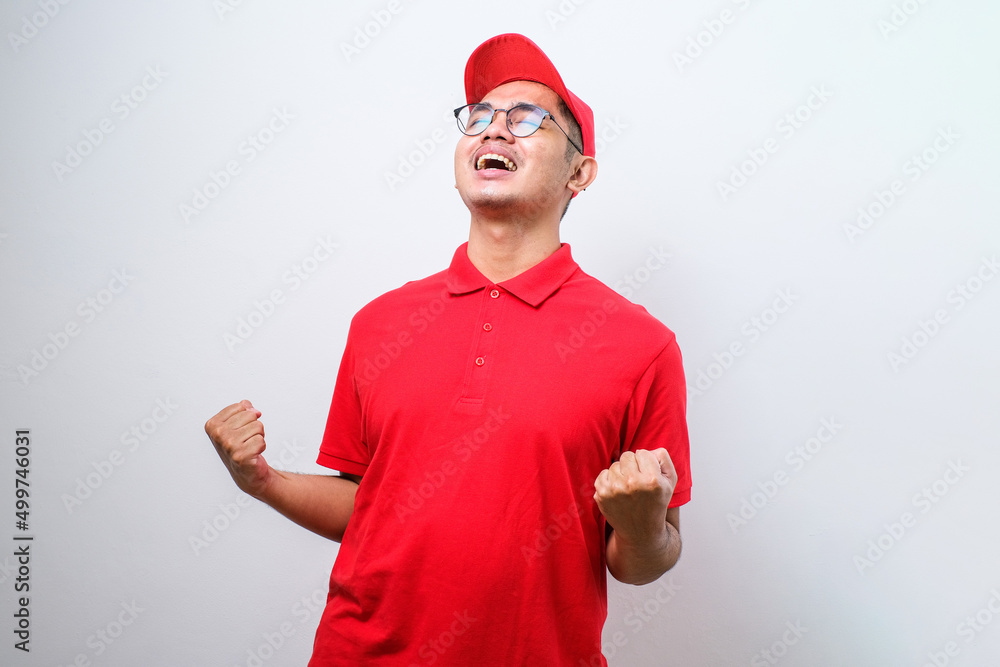 Asian delivery man very happy and excited doing winner gesture with arms raised, smiling and screaming for success. Asian delivery man very happy and excited doing winner gesture with arms raised, smiling and screaming for success.