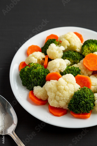Mixed Organic Steamed Vegetables (Carrots, Broccoli and Cauliflower) on a Plate on a black surface, side view.
