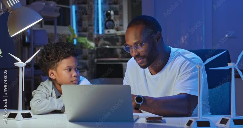 African american businessman and father using computer teaching and explains to his son how wind turbines work. Kids learning about eco-friendly forms of renewable energy. Technology and education.