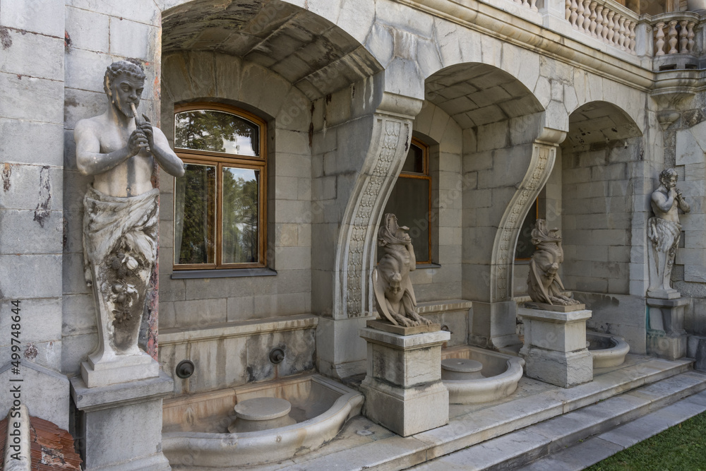 Ancient statues near the walls of the historical Massandra Palace (Yalta, Crimea) in summer. close-up of the details of the facade. Stone satyrs and chimeras, water bowls as exterior decoration