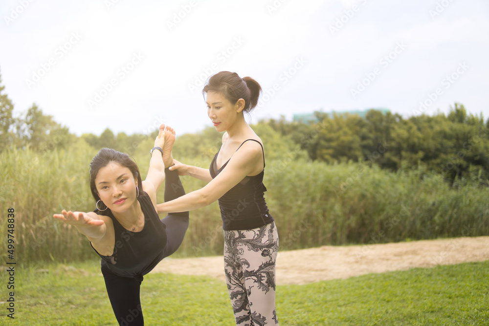 Obraz premium Two young Asian women practicing yoga outdoors. 