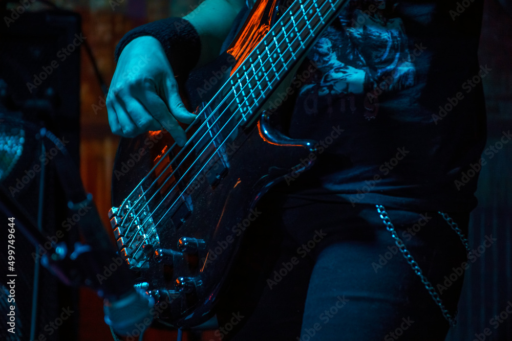 The bass guitarist plays the bass guitar. Dark key. Selective focus - obrazy, fototapety, plakaty 
