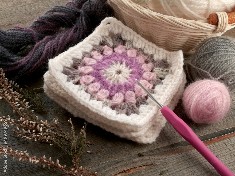 Handmade crocheting granny square, a hook and yarn balls on old wooden table Handmade crocheting granny square, a hook and yarn balls on old wooden table