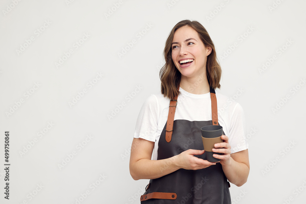 Portrait of beautiful young barista woman looking left and smiling or laughing, while holding a to-go coffee in hand. Isolated on white background. Portrait of beautiful young barista woman looking left and smiling or laughing, while holding a to-go coffee in hand. Isolated on white background.
