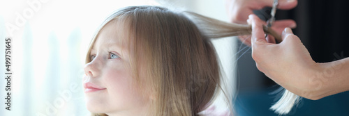 Hairdresser cutting hair of little girl in beauty salon