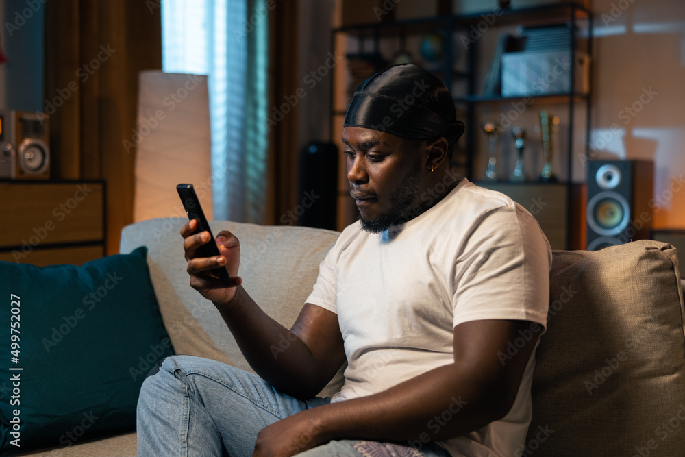 Bored young boy, student is relaxing on couch in evening with phone, smartphone in hand. Man lies on the couch and sends messages to friends, browses social media, likes to comment on posts. Bored young boy, student is relaxing on couch in evening with phone, smartphone in hand. Man lies on the couch and sends messages to friends, browses social media, likes to comment on posts.
