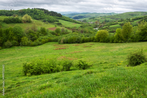 carpathian countryside landscape in spring. grassy meadows, rural fields and forested slopes on hills rolling off in to the distant village in the valley. overcast rainy weather with above the ridge