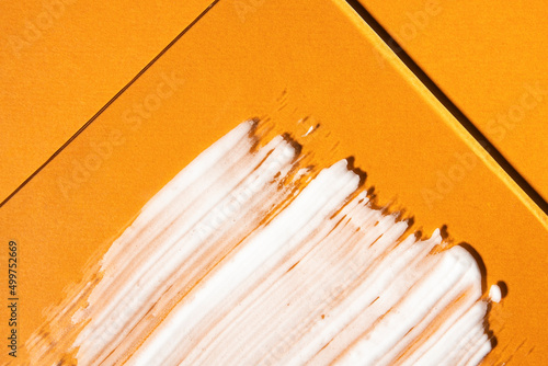 White colored sunscreen on a bright orange background, top view. Summer sun protection product, close-up smear.