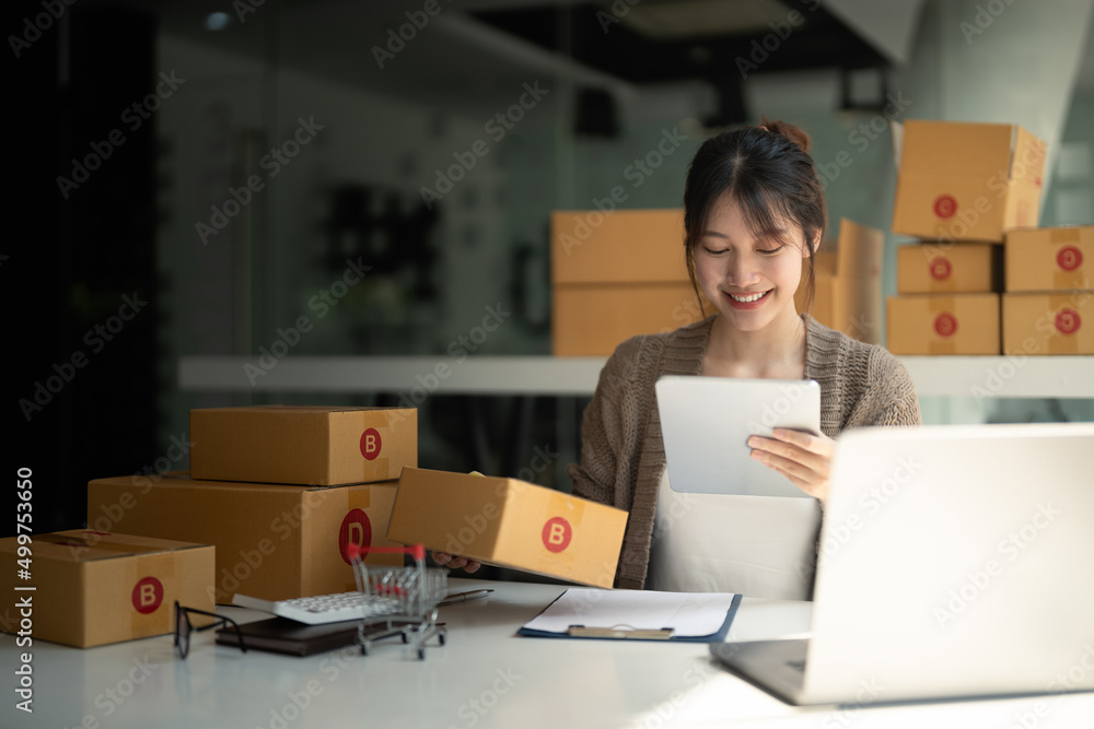 Young woman small business owner online shopping at home. checking orders from customers with digital tablet preparing package product on background. SME entrepreneur or freelance concept Young woman small business owner online shopping at home. checking orders from customers with digital tablet preparing package product on background. SME entrepreneur or freelance concept