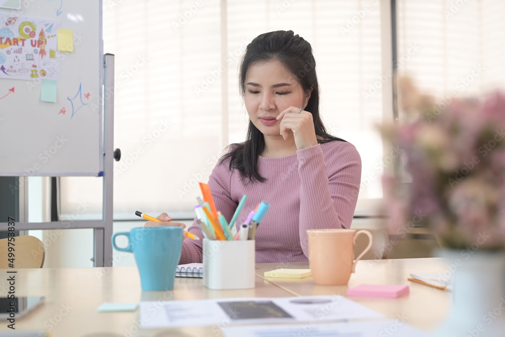 Concentrated young creative woman sitting at her office desk and making notes of important data. Concentrated young creative woman sitting at her office desk and making notes of important data.