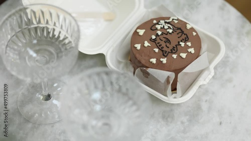 Chocolate bento cake in eco box with wooden spoon. White candle and chmpagne glasses on luxury marble table photo