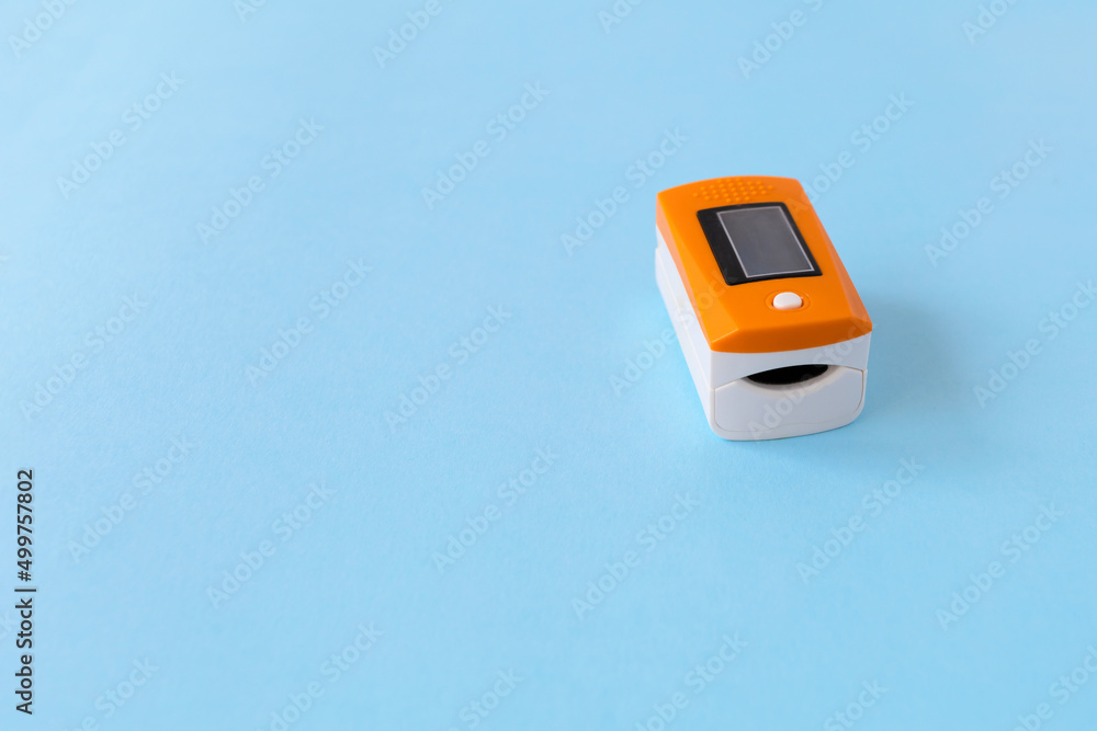 orange pulse oximeter on finger on blue background, copy space, place for text. portable device instrument for measuring saturation, oxygen in the blood orange pulse oximeter on finger on blue background, copy space, place for text. portable device instrument for measuring saturation, oxygen in the blood