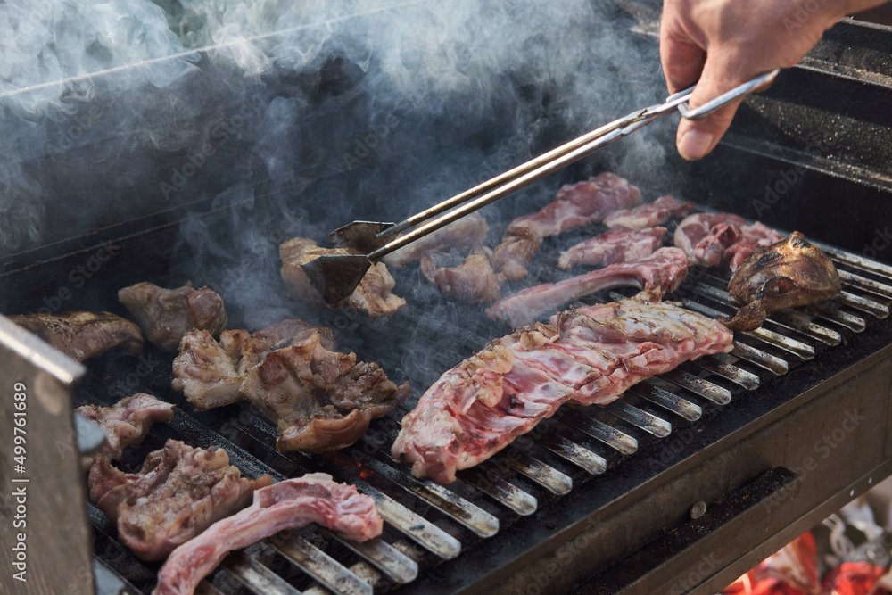 A man cooking ribs on barbecue grill for summer outdoor party. BBQ smoke. Food background.