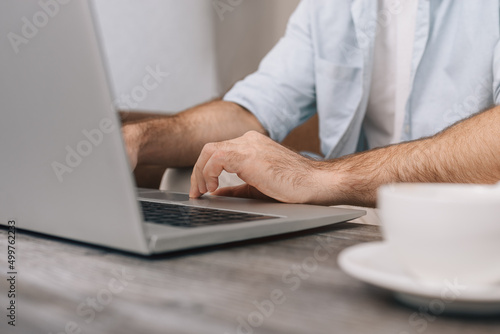 Hands of a modern young programmer or office manager over a laptop keyboard while programming. A guy in a blue shirt and white T-shirt. Cup of coffee on the table. Freelance