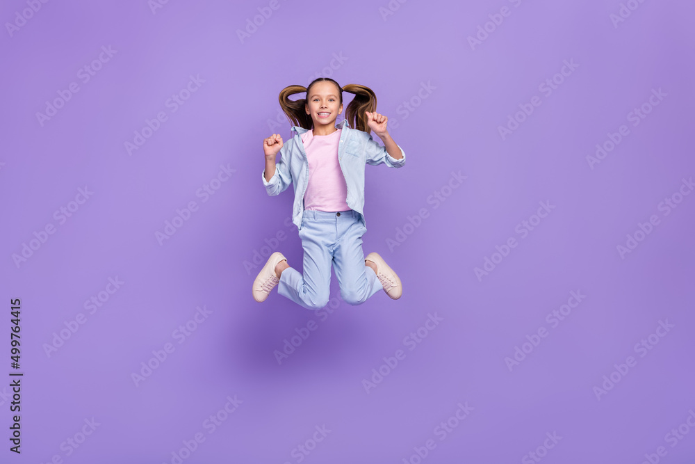 Photo of sweet lucky small schoolgirl dressed jeans shirt jumping high rising fists isolated violet color background Photo of sweet lucky small schoolgirl dressed jeans shirt jumping high rising fists isolated violet color background