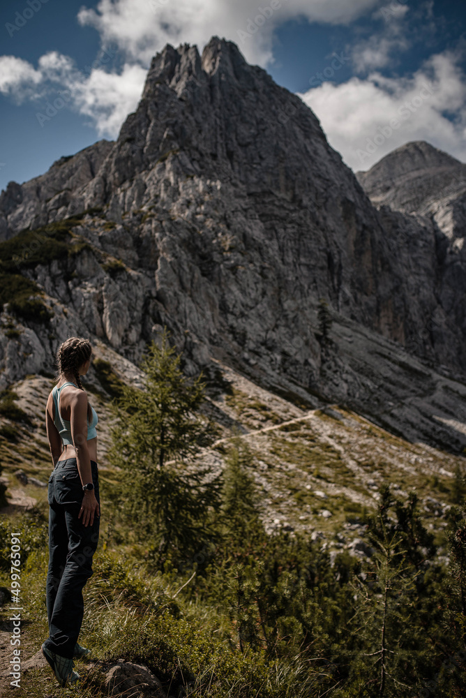 Young woman wearing braids is enjoying beautiful view of both Mala and Velika Mojstrovka in Slovenia during a late summer hike in Julian Alps