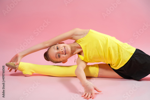 Young gymnast girl stretching and training on a pink background. Sport and healthy lifestyle concept