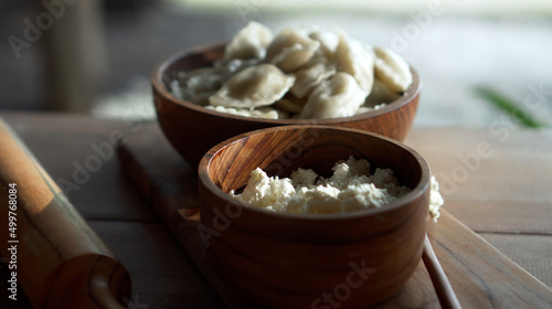 Russian fresh handmade dumplings lying on a wooden table on a cutting board with cottage cheese in a wooden plate