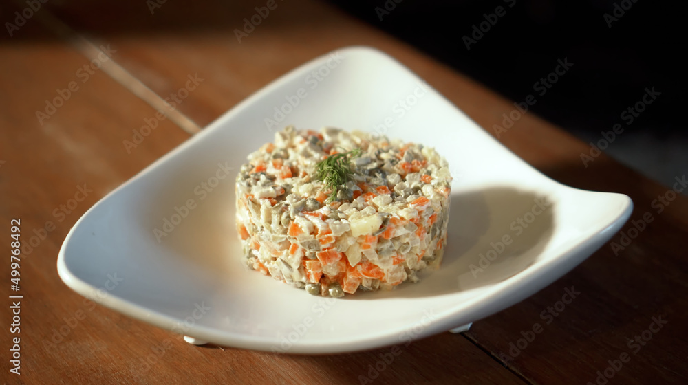 Traditional Russian fresh olivier salad lying on a wooden table