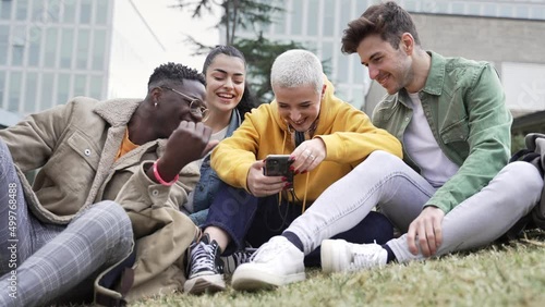 Happy University student friends having fun sharing moments on smartphone app sitting on the campus grass photo