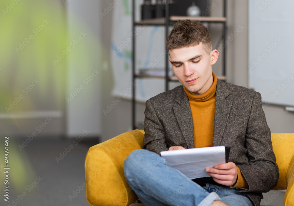 handsome young man fills out a form sitting in the office on a chair handsome young man fills out a form sitting in the office on a chair