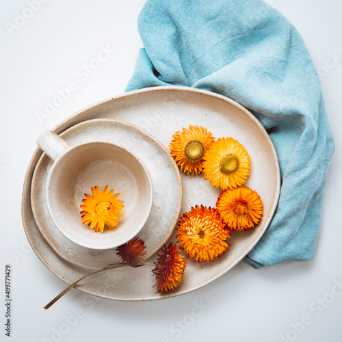 Overhead view of orange springtime strawflower flower heads on a ceramic plate with a cup and saucer photo