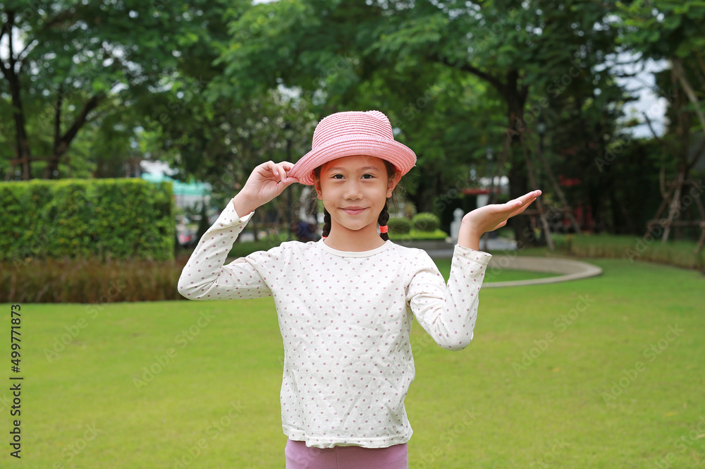 Portrait of Asian young girl kid standing with her hand up present something on empty space in the garden.