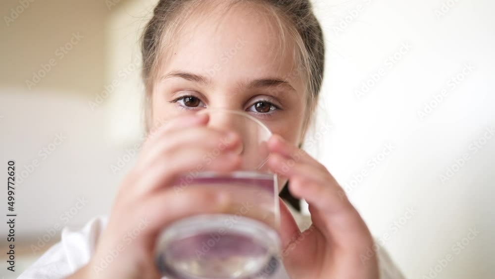child girl drinking water from a glass cup. the problem of lack of clean drinking water lifestyle in the world. little girl in the kitchen drinks drinking water from a transparent glass cup
