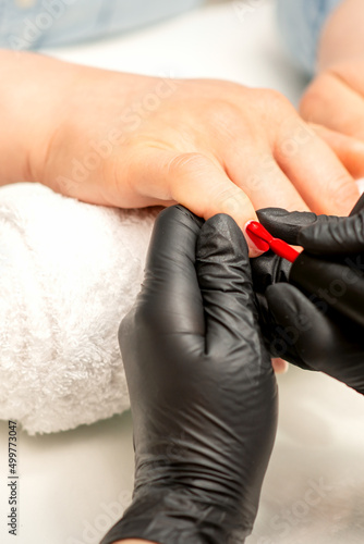 Manicure varnish painting. Close-up of a manicure master wearing rubber black gloves applying red varnish on a female fingernail in the beauty salon