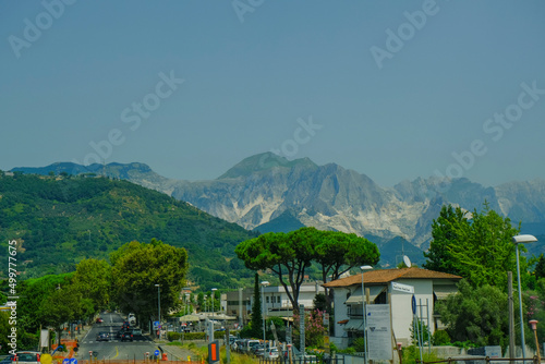 Backdrop of the Apuane mountains in Tuscany, Marina di Carrara, Italy. Mountains landscape with pines, city streets across blue sky  