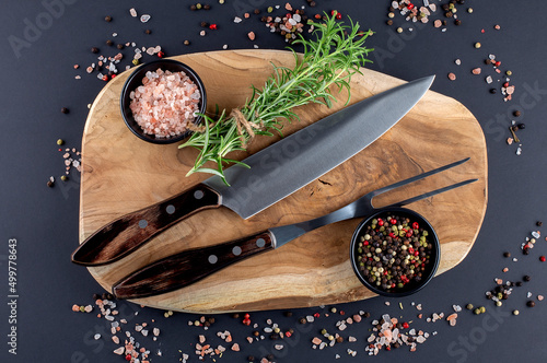 Wooden cutting board, rosemary and spices with fork and knife carving set on dark background photo