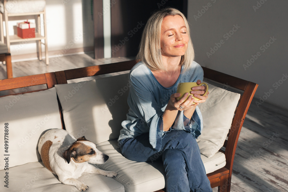 Obraz premium Adult woman sitting on the sofa at home and having a cup of coffee