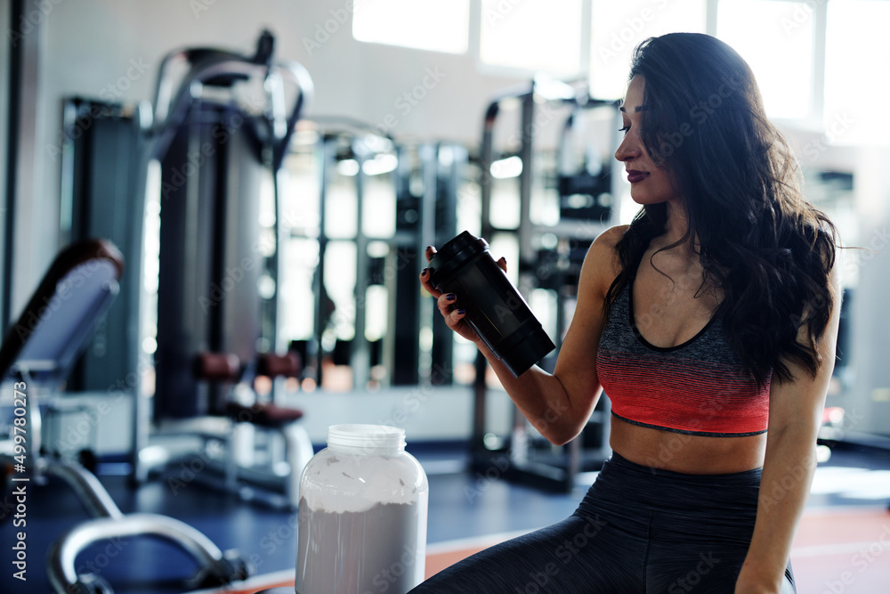 Fototapeta premium Young active woman taking a break in a gym with protein shake.