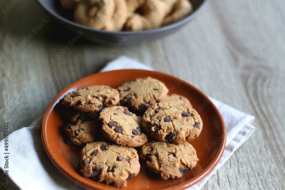Plate of chocolate chip cookies and bowl of sugar cookies on wooden table. Selective focus. Plate of chocolate chip cookies and bowl of sugar cookies on wooden table. Selective focus.