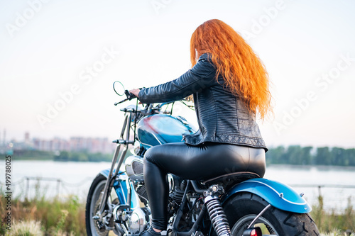 Fototapeta Rear view of red-haired curly woman in leather clothing motorcycle outdoors