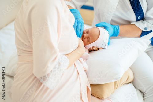 Breastfeeding advice concept. Female breastfeeding consultant supports young mother, help her comfort breastfeeding baby using pillow.