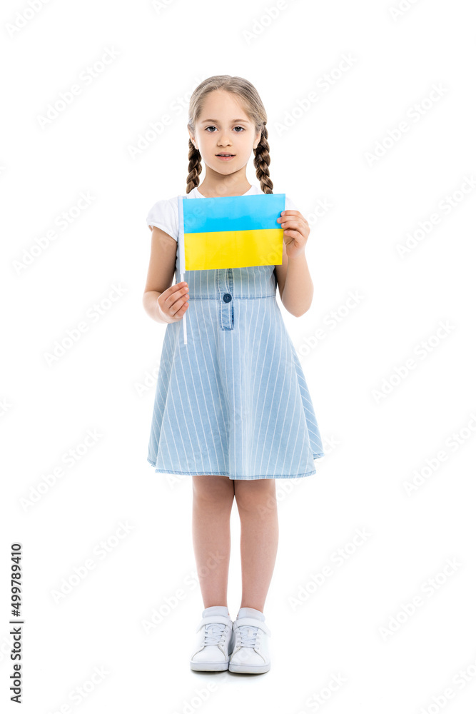 full length view of girl in blue dress holding small ukrainian flag on white. full length view of girl in blue dress holding small ukrainian flag on white.