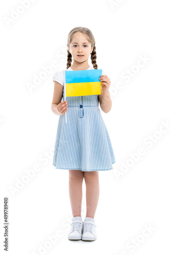 full length view of girl in blue dress holding small ukrainian flag on white.