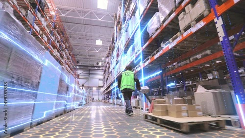 Digitalization of production. A worker is carrying a rokla through a large warehouse. The worker walks through the warehouse. Futuristic production concept.