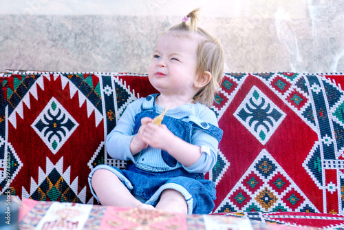 Happy child in a street cafe. Baby loves gozleme very much. Funny girl in an authentic restaurant. The kid has a snack on the dastarkhan photo