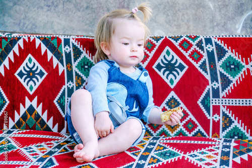 The kid has a snack on the dastarkhan. Happy child in a street cafe. Baby loves gozleme very much. Funny girl in an authentic restaurant photo