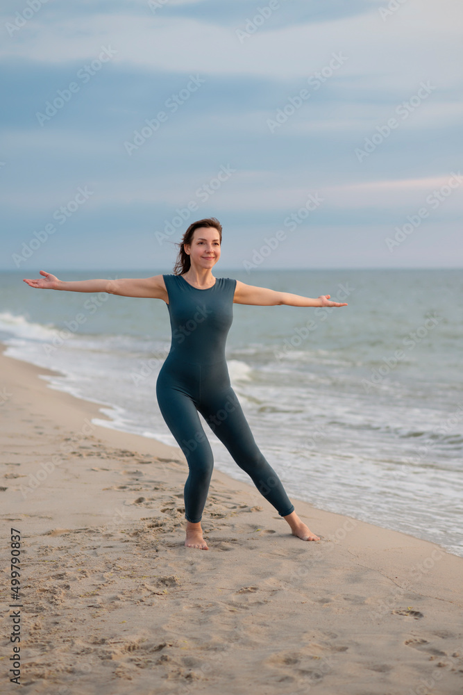 Woman in a blue sports jumpsuit does gymnastics on the seashore Woman in a blue sports jumpsuit does gymnastics on the seashore