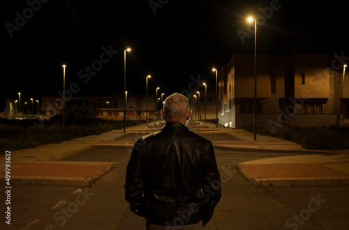 Rear view of adult man walking on street at night