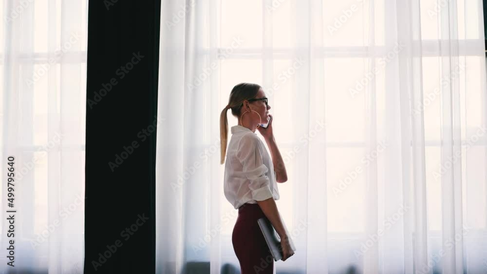 4k Elegant businesswoman in glasses and white shirt. Talking on the phone near big office window. 4k Elegant businesswoman in glasses and white shirt. Talking on the phone near big office window.
