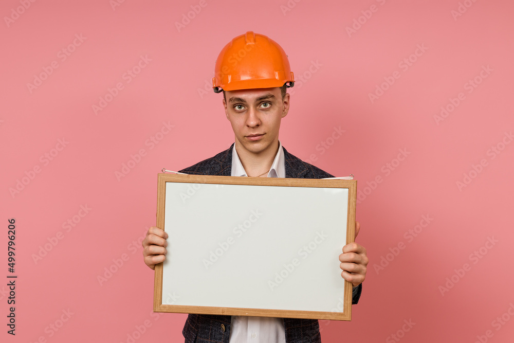 young engineer in a protective helmet and jacket with a white board in his hands on a pink background young engineer in a protective helmet and jacket with a white board in his hands on a pink background