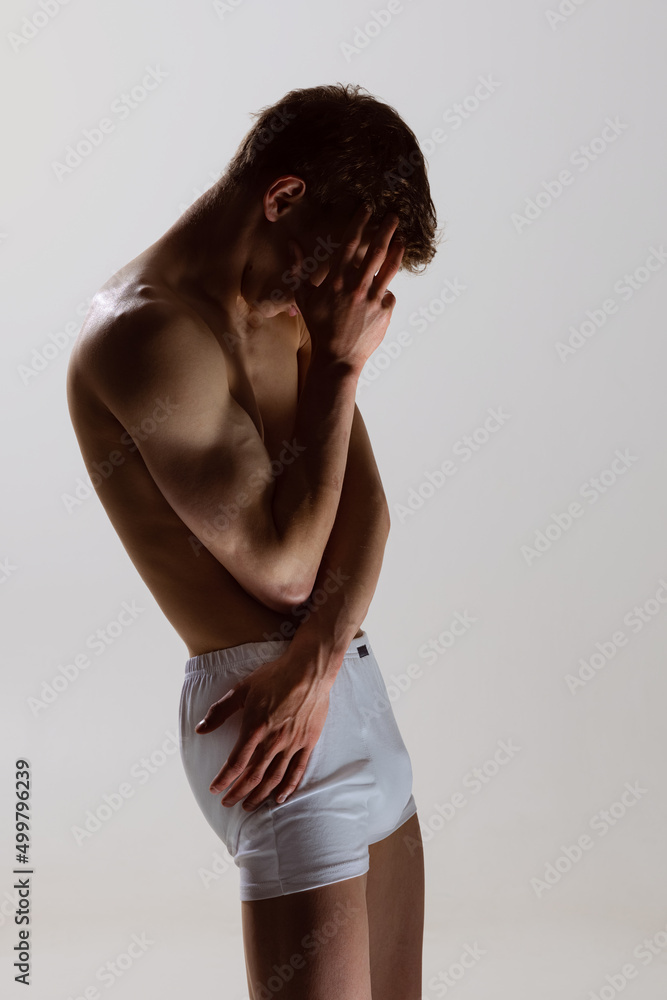 Close-up portrait of young handsome shirtless muscled man wearing white boxer-briefs standing isolated on gray background. Natural beauty of male body Close-up portrait of young handsome shirtless muscled man wearing white boxer-briefs standing isolated on gray background. Natural beauty of male body