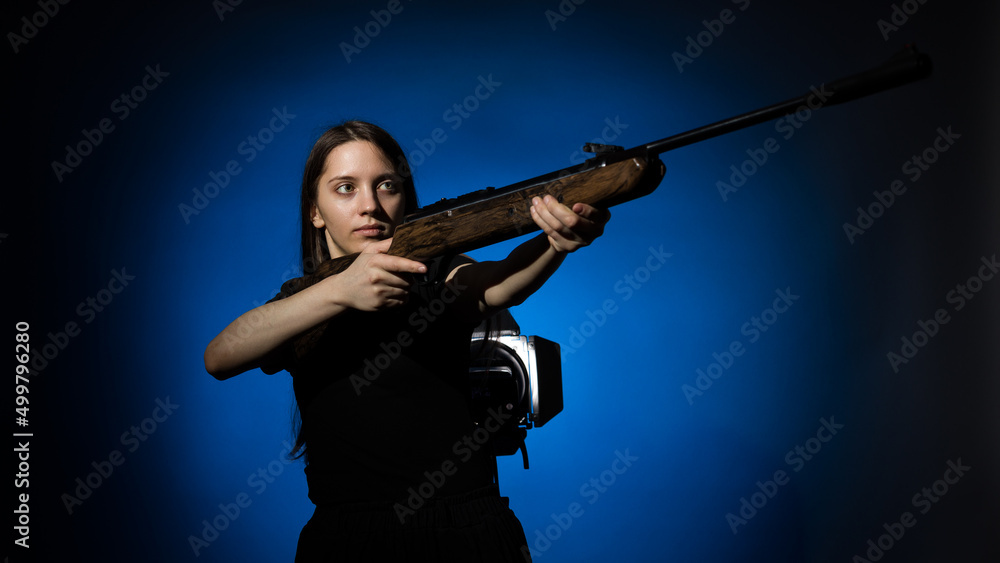 a young girl with long flowing hair in a black T-shirt aims a gun on a dark background