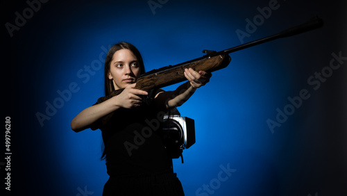 a young girl with long flowing hair in a black T-shirt aims a gun on a dark background