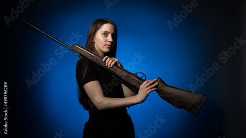 a young girl with long flowing hair in a black T-shirt with a gun on her shoulder on a dark background