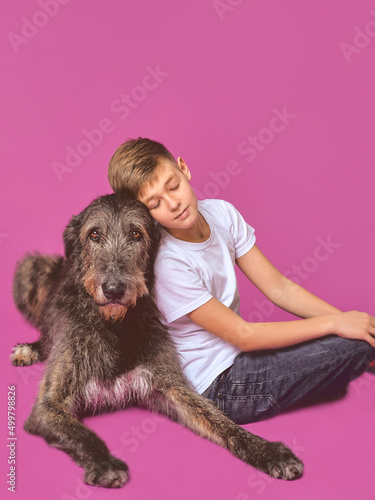 Smiling cheerful eleven years teen in white t-shirt and jeans with brown big dog on fuchsia color background in photo studio. Pets, friendship concept